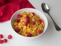 Cornflakes breakfast cereal with raspberries in bowl on white ta