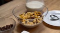 Cornflakes with chocolate balls and milk in a glass bowl on a wooden table with a jug of milk and a plate with a spoon Royalty Free Stock Photo