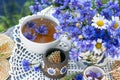 Cornflower herbal tea in white cup on white crochet napkin on wooden table outdoors, healthy cornflower drink with honey