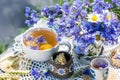 Cornflower herbal tea in white cup on white crochet napkin on wooden table outdoors