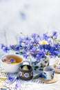 Cornflower herbal tea in white cup on white crochet napkin on wooden table outdoors