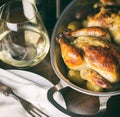 Cornish hens in an aluminum baking pan right out of the oven, shown with stemless glass of white wine and vintage fork on napkin. Royalty Free Stock Photo