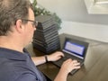 A casually dressed caucasian middle aged man is installing a laptop computer with a stack of several more computers next