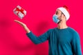 Corona virus christmas concept. young man with santa claus hat and face mask and gifts in studio with red background, happy Royalty Free Stock Photo