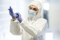 Corona virus concept. Male scientist doctor in mask, glasses and protective suit putting on latex gloves and getting Royalty Free Stock Photo