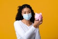 Coronacrisis Concept. Upset black worry woman in medical face mask holding piggybank