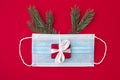 Coronavirus christmas concept made from face mask, fir tree, gift box and decorations on red background. flat lay Royalty Free Stock Photo