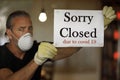 Coronavirus closed for business concept, male with medical mask puts sorry closed sign on window due to covid 19 pandemic