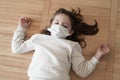 Coronavirus covid-19 epidemic outbreak concept of little suffering girl with medical mask lying on floor at home