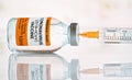 Coronavirus covid-19 vaccine concept - glass bottle with silver cap on glossy white desk, orange syringe hypodermic needle