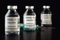 Coronavirus Covid-19 vaccine concept - three glass vials on black table, hypodermic syringe needle near, closeup detail label