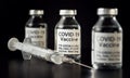 Coronavirus Covid-19 vaccine concept -  three glass vials on black table, hypodermic syringe needle near, closeup detail label Royalty Free Stock Photo