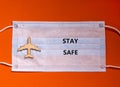 Coronavirus flight cancellations concept. Face mask and airplane toy on orange background. Words `stay safe`. Copy space