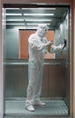 Coronavirus infection. Paramedic in protective mask and costume disinfecting an elevator with sprayer,