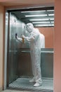 Coronavirus infection. Paramedic in protective mask and costume disinfecting an elevator with sprayer, Royalty Free Stock Photo