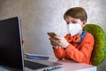 Coronavirus Outbreak. Lockdown and school closures. School boy with face mask watching online education classes feeling bored and Royalty Free Stock Photo