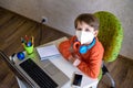 Coronavirus Outbreak. Lockdown and school closures. School boy with face mask watching online education classes feeling bored and Royalty Free Stock Photo