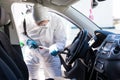 Coronavirus Pandemic. Disinfector in a protective suit and mask sprays disinfectants of car outdoors