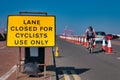 A cyclist approaches a yellow sign advising that a road lane is closed to cars