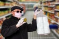 Coronavirus panic concept. Man with surgical mask, hood, glasses and medical gloves shows a package of toilet paper and an