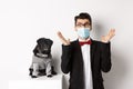 Coronavirus, pets and celebration concept. Amazed young man in face mask and suit staring at camera surprised, cute