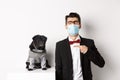 Coronavirus, pets and celebration concept. Disappointed young man in face mask and suit, pointing finger at cute black