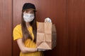 Coronavirus and quarantine. Safe food delivery from restaurants. Young woman courier in uniform in a medical antibacterial mask Royalty Free Stock Photo
