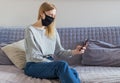 Coronavirus. Woman in quarantine for covid wearing protective mask, she working from home and using mobile phone at sofa