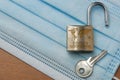 Coronavirus world lockdown end: an open lock with a world map and the word lockdown engraved and a key on a light blue surgical Royalty Free Stock Photo