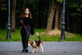 Coronavirus.Young caucasian woman with face mask takes his dog for a walk in the park during Covid-19 restrictions