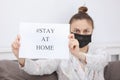 Coronavirus. Young woman in protection mask holding paper with Stay Home in her house. isolated to prevent infection of pandemic,