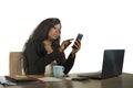 Young beautiful and busy black afro American businesswoman using mobile phone working on desk with laptop computer at company Royalty Free Stock Photo