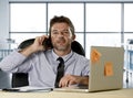 Corporate portrait of happy successful businessman in shirt and tie smiling at computer desk with mobile phone