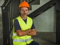 Corporate portrait of young attractive and happy builder man or constructor posing confident smiling wearing building helmet and