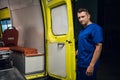 Corpsman in blue uniform stands and looks at camera in the ambulance car