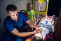 Corpsman in medical uniform holds a mask on woman liyng on stretcher, little sad girl sits beside her