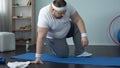 Corpulent man sitting on mat for exercising, labored breathing, obesity problems