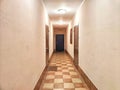 A corridor with wooden doors and a checkered floor pattern. Warmly Lit Hotel Corridor With Checkered Floor Design Royalty Free Stock Photo