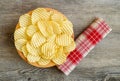 Corrugated golden potato chips in a wooden bowl on rustic wooden table.