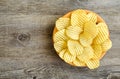 Corrugated golden potato chips in a wooden bowl on rustic wooden table.