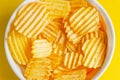 Corrugated potato chips in a white plate on a beautiful yellow background. close-up, details.