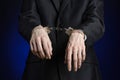 Corruption and bribery theme: businessman in a black suit with handcuffs on his hands on a dark blue background in studio isolated Royalty Free Stock Photo