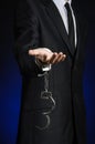 Corruption and bribery theme: businessman in a black suit with handcuffs on his hands on a dark blue background in studio isolated