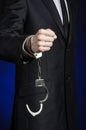 Corruption and bribery theme: businessman in a black suit with handcuffs on his hands on a dark blue background in studio isolated