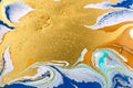 Cose up gold glitter wave on liquid blue and white paint background.