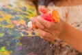 Cose up of woman hand with orange flask, over a color palette in a blurred background