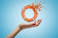 Cose-up of woman`s hand facing up and levitating miniatured orange lifebuoy which started dissolving into small pieces