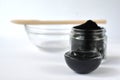 Cosmetic activated carbon charcoal powder in a glass jar and beauty face mask mixture on white with copy space.