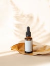 Cosmetic amber glass bottle with white lable on dry leaf on beige background with plant shadow