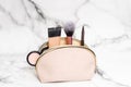 Cosmetic bag on a marble background with a makeup brush, tonal foundation, liner, blush and eye shadow